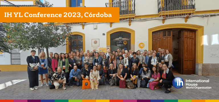 A large group of people poses for a photo outside a building at the IH YL Conference 2023 in Córdoba, under a banner with the event name.