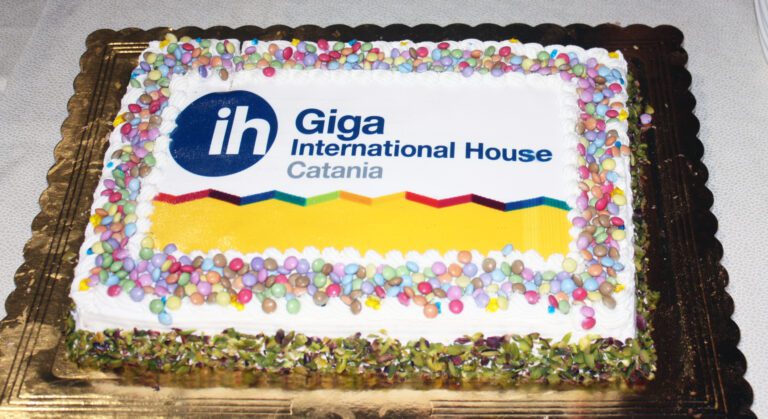 A rectangular cake decorated with colorful candy and the logo of Giga International House Catania printed on top.