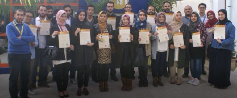 A group of people, some holding certificates, stand together and face the camera for a group photo indoors.
