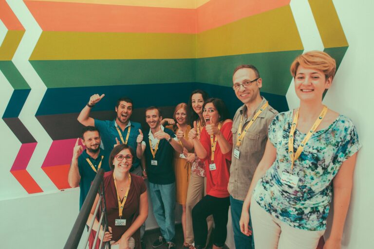 Nine people wearing name badges pose and smile on a staircase in front of a colorful geometric wall mural.