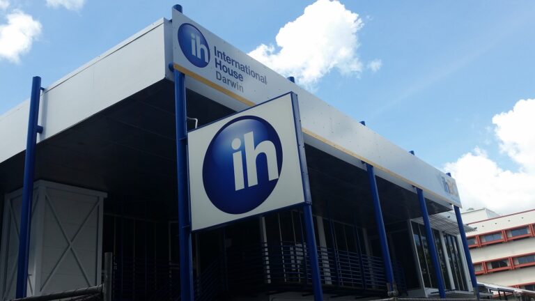 Modern building with "International House Darwin" signage and large "ih" logo on two signs, viewed from below against a partly cloudy sky.