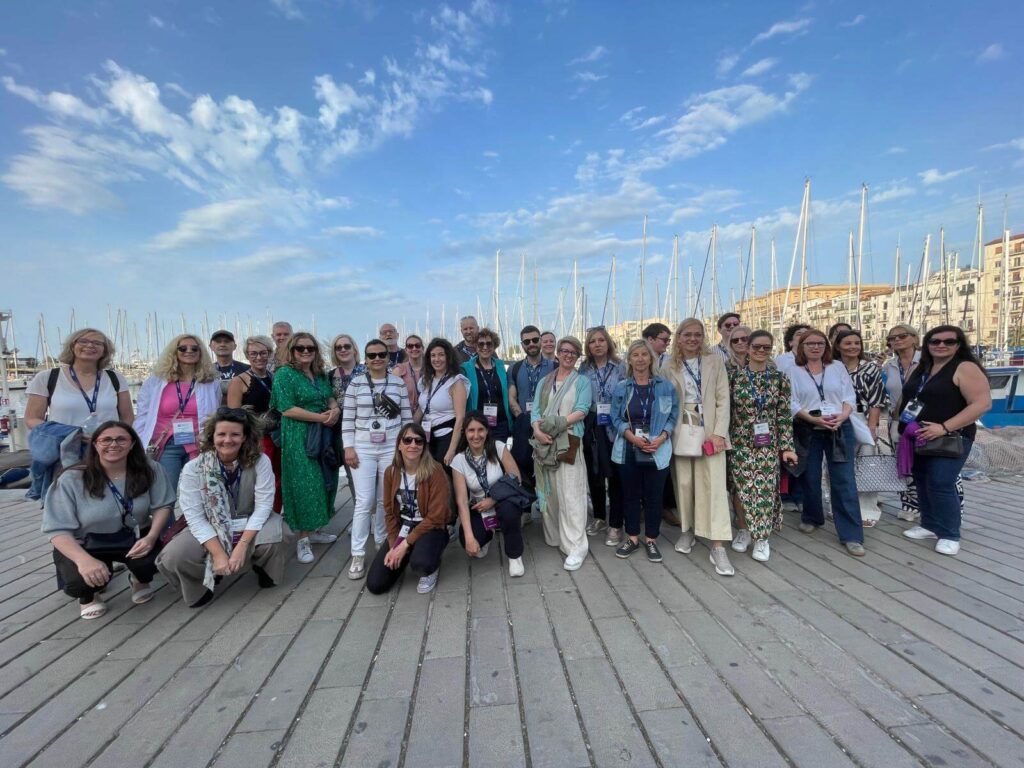 A group of people pose for a photo on a dock with sailboats and buildings in the background under a partly cloudy sky at the International House study abroad event.