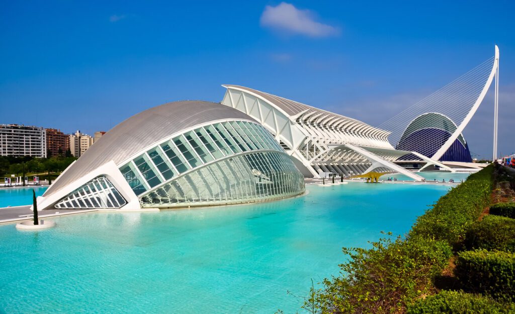 Futuristic white buildings with glass facades surrounded by turquoise water at the City of Arts and Sciences in Valencia, Spain, under a clear blue sky.