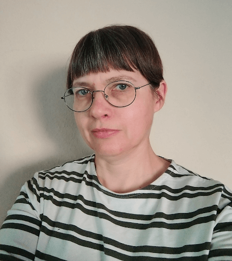 Woman with a fringe and glasses wearing stripy top smiles slightly at the camera.