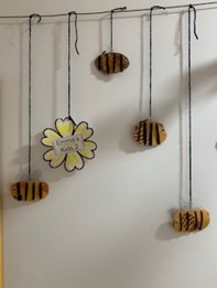 Four bee-shaped ornaments and a flower-shaped sign labeled "Bumble Bee Rules" hang from strings against a white wall.