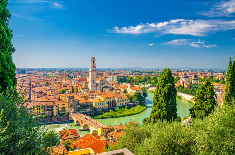 A view of Verona o a sunny day, blue skies and the sun shines on the tower and orange roofs.