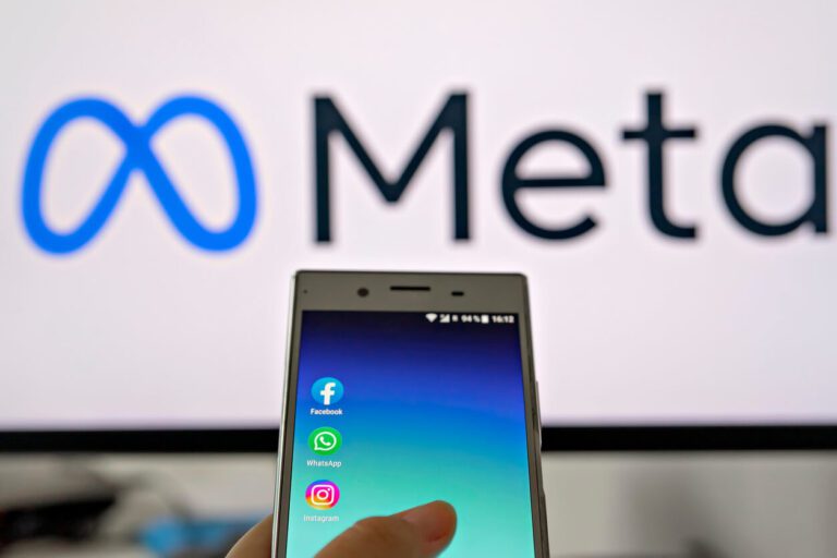 A hand holds a smartphone displaying Facebook, WhatsApp, and Instagram apps, with the Meta logo and name visible in the background.