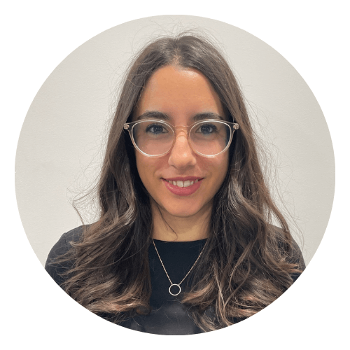 Glamorous Spanish woman with wavy brown hair and transparent framed glasses smiles at the camera