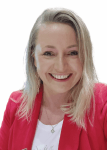 A woman with blonde hair, wearing a red blazer, white top, and dangling earrings, smiles at the camera against a plain white background.
